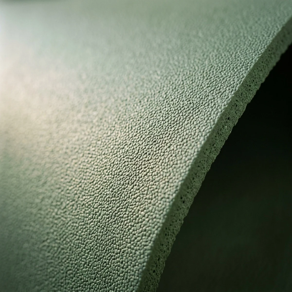 Macro detail of a sage natural rubber mat — fine matte micro-pebbled grip texture at a cleanly cut edge